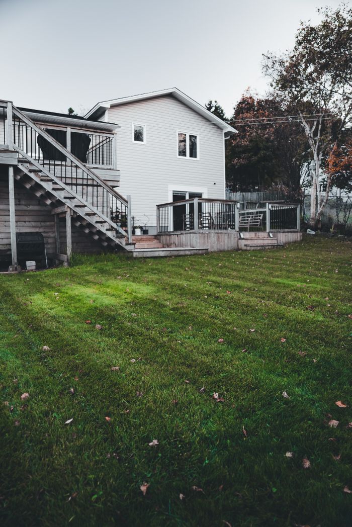 hero-img-02 White house with a wooden deck overlooking a well-maintained spacious green backyard.